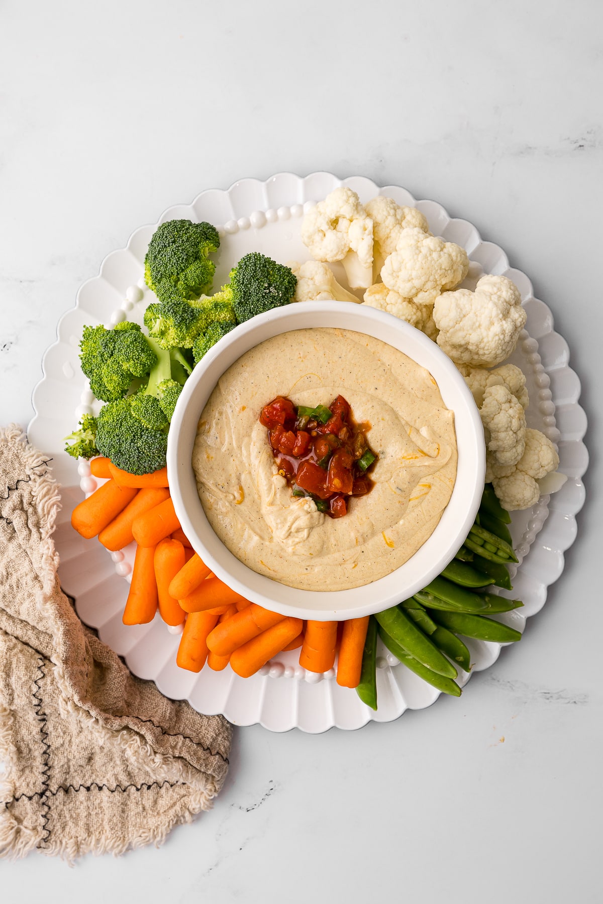 overhead photo of cottage cheese queso in a white bowl surrounded by fresh vegetables