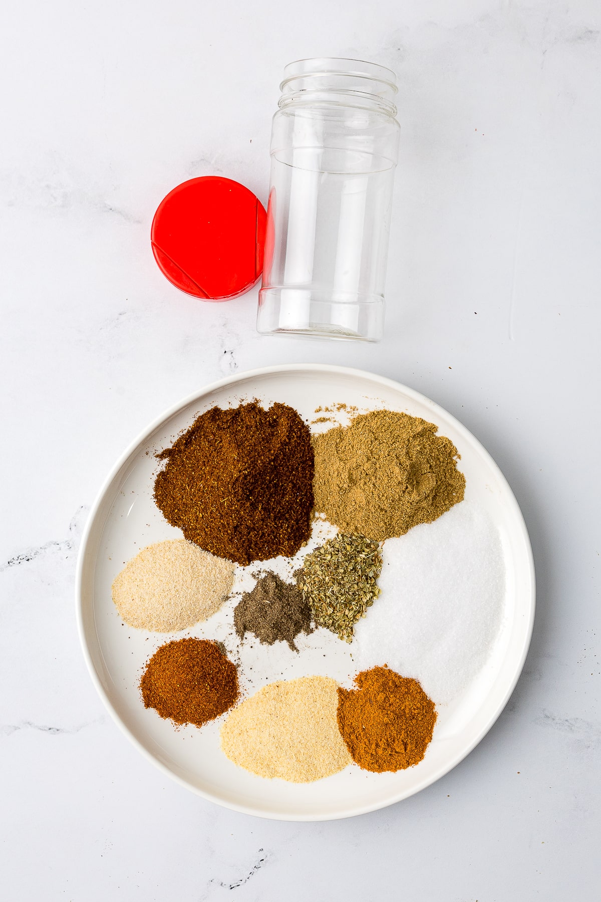 spice piles on a white plate with an empty spice jar on a white marble countertop