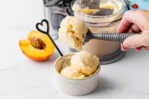 scooping peach ice cream into an ice cream bowl with a heart spoon, peaches and a pint jar in the background