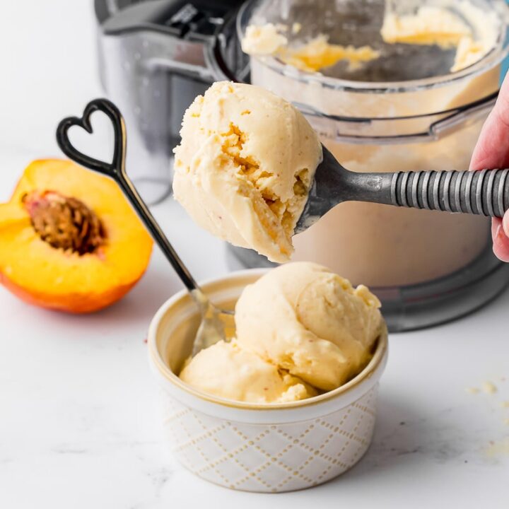 scooping peach ice cream into an ice cream bowl with a heart spoon, peaches and a pint jar in the background