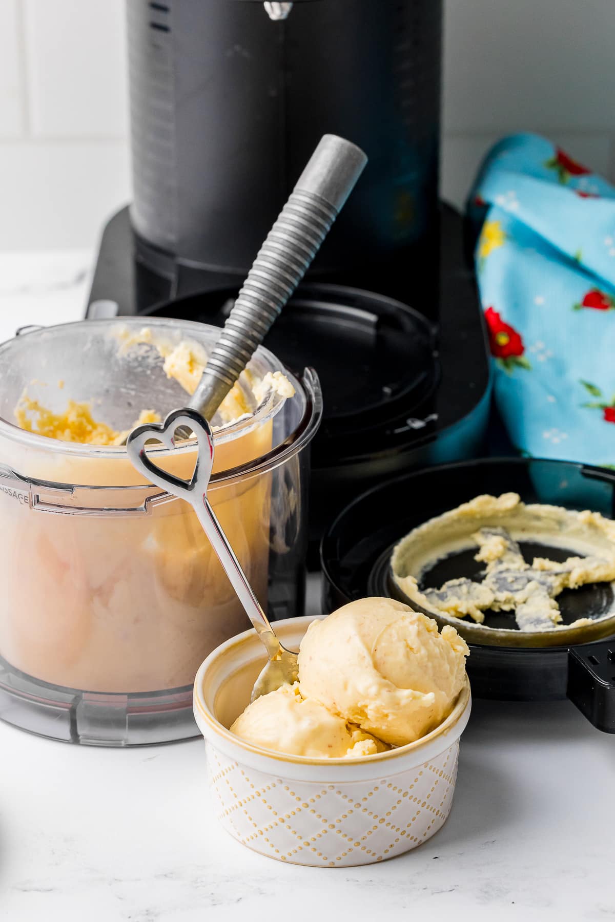 peach ice cream in an ice cream bowl with a heart spoon and a ninja creami in the background