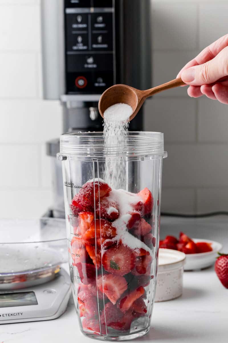 pouring sugar over strawberries with a ninja creami ice cream maker in the background