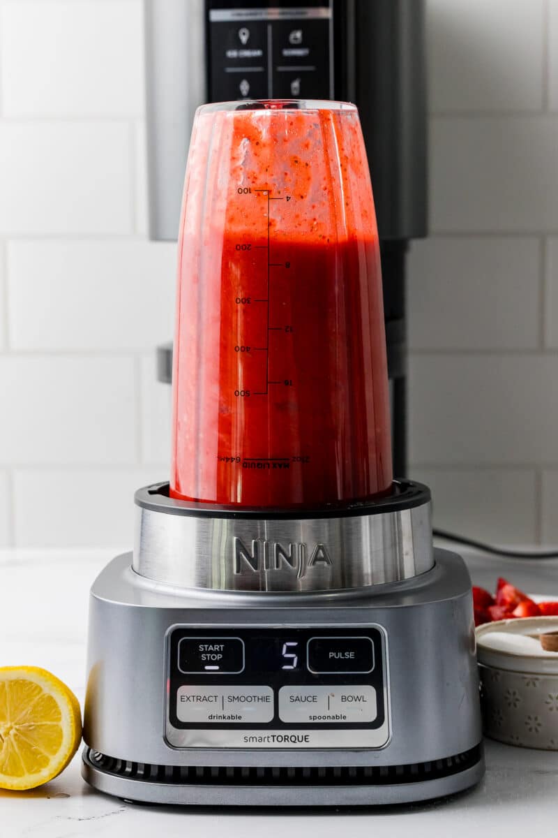 ninja smart torque blending strawberry sorbet mixture on a white counter with half a lemon beside the machine