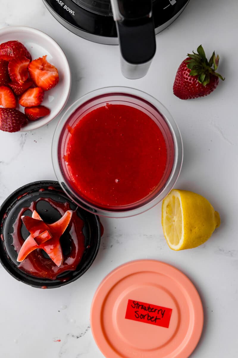 ninja creami pint jar filled with strawberry sorbet with a half a sliced lemon and fresh strawberries in a bowl