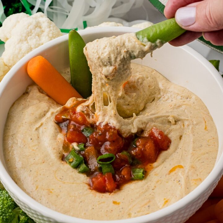 sugar snap pea dipped in cottage cheese queso surrounded by fresh vegetables