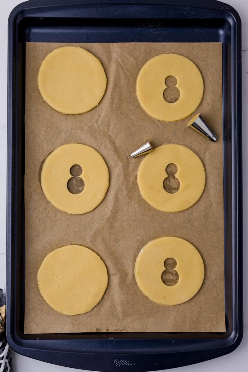 round sugar cookie dough with spider bodies cut out on a cookie sheet