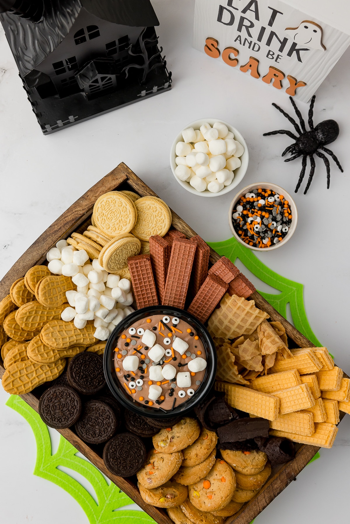 Party tray of cookies on a wooden tray with a bowl of chocolate dip in the middle of Halloween party decor