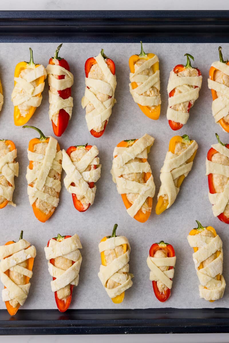 unbaked halloween poppers in a baking sheet lined with parchment paper and a wilton bat spatula