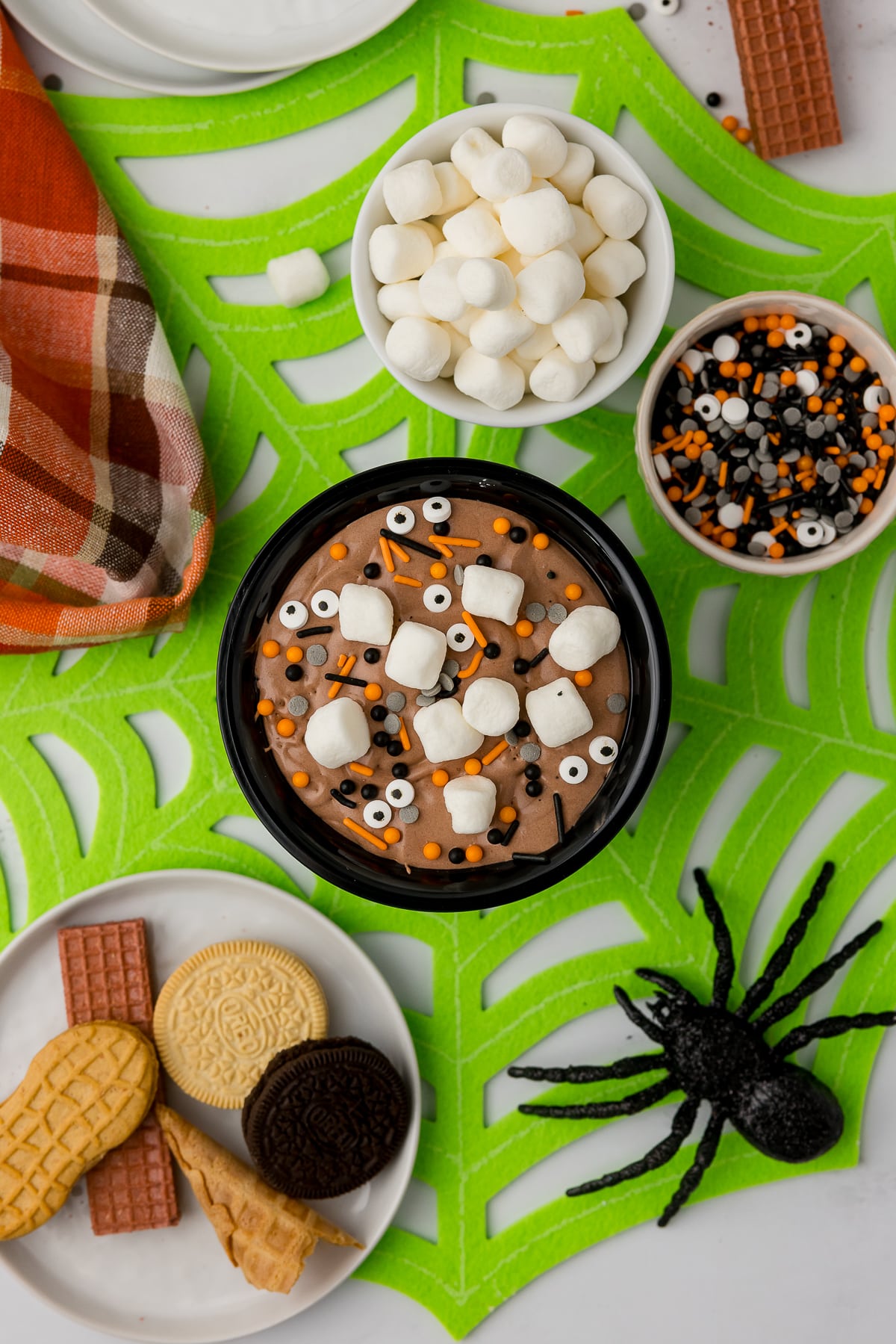 Halloween party table with festive decor including a spooky spider, Halloween sprinkles, candy eyes and cookies