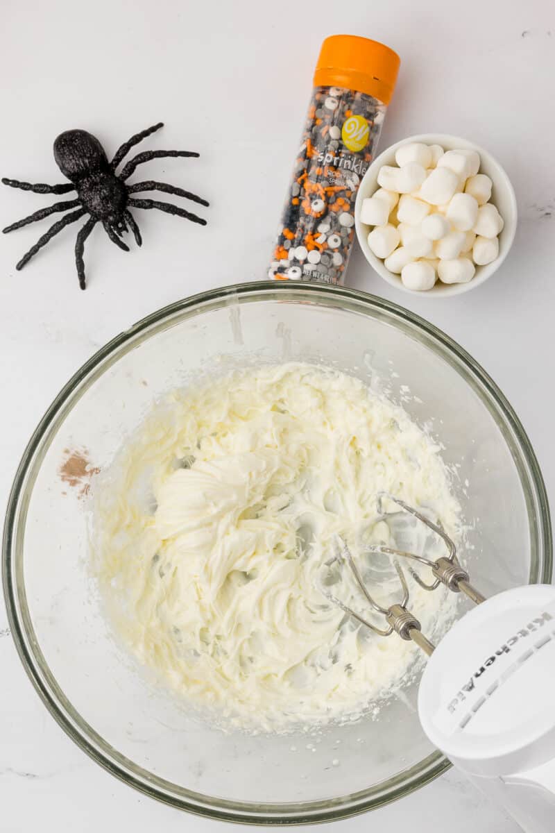 Blending up frosting in a clear glass bowl with a Halloween spider and spooky sprinkles