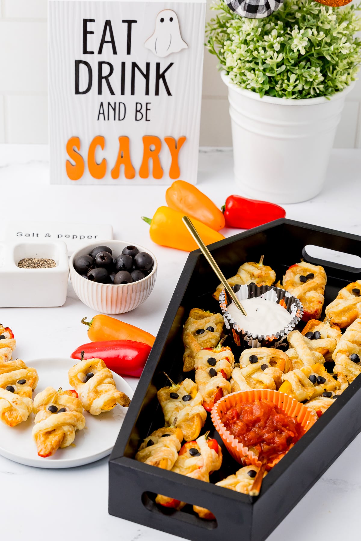 easy halloween appetizers made from pastry wrapped poppers in a black coffin tray with peppers, a plant and a sign that says Eat, Drink, and be Scary