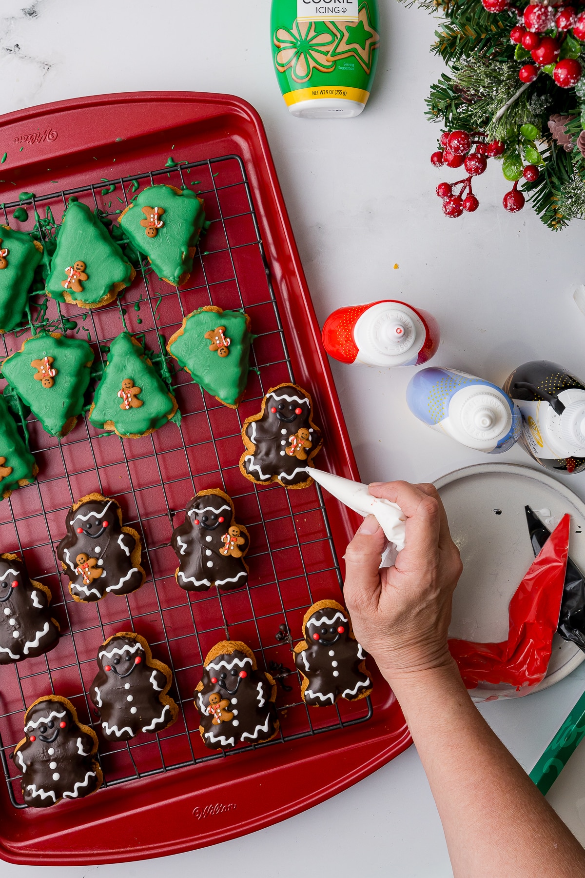 A hand putting white icing decorations on a chocolate dipped cookie on a baking tray