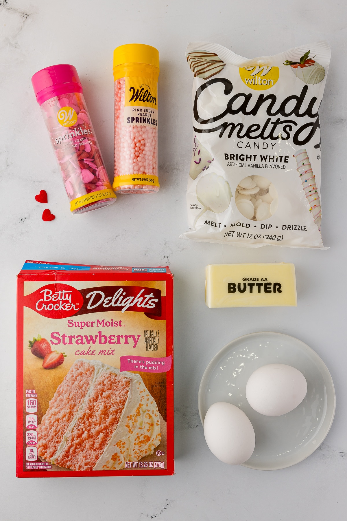 Wilton sprinkles, wilton candy melts in bright white, betty crocker strawberry cake mix, a stick of butter, and 2 eggs