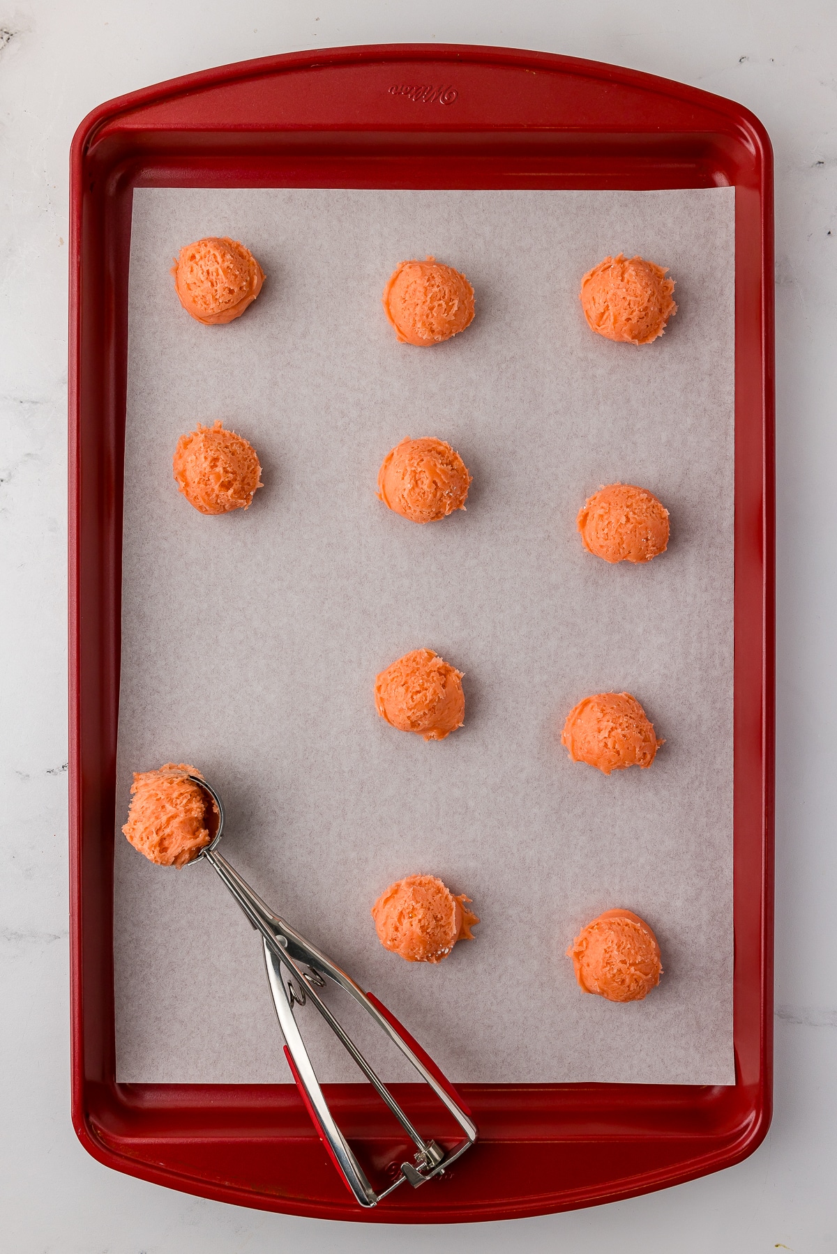 red cookie sheet with parchment paper sheet, and dough balls