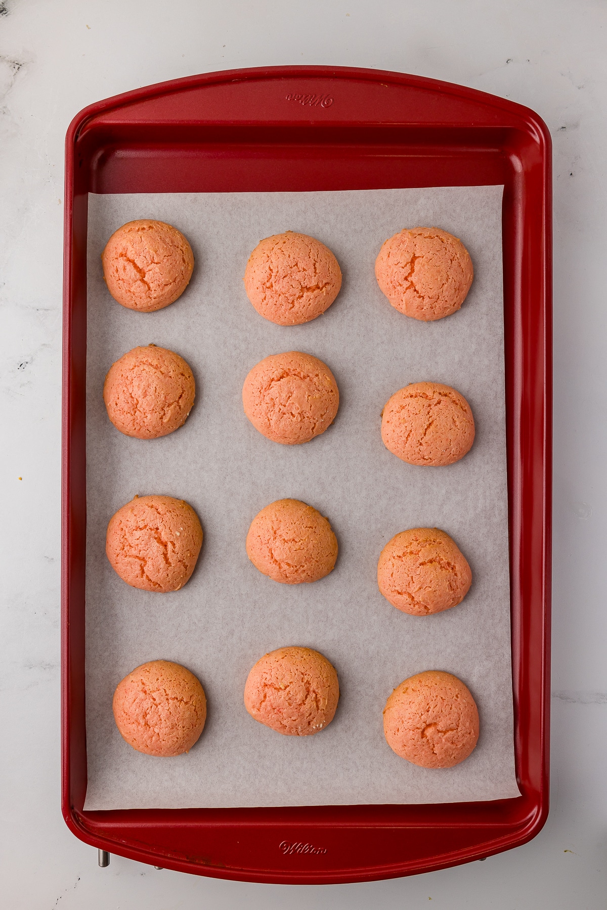 cooked strawberry cake mix cookies on a red wilton cookie sheet