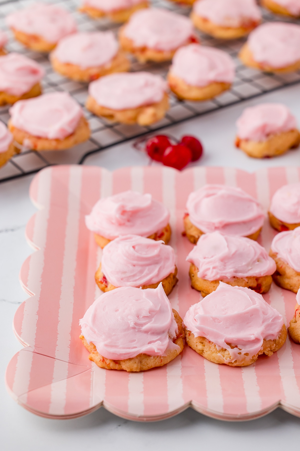 cherry cookies with pink frosting on a scalloped plate