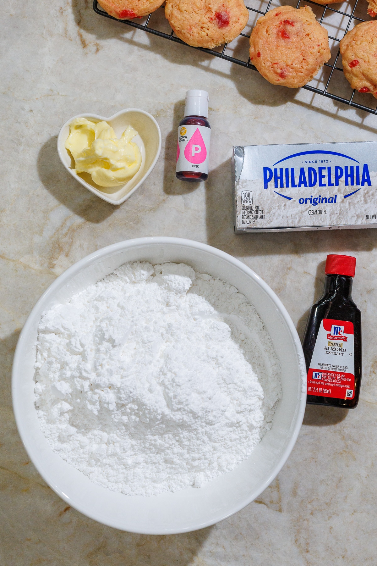 powdered sugar in a bowl with butter, philadelphia cream cheese, almond extract and cherry cookies on a white countertop