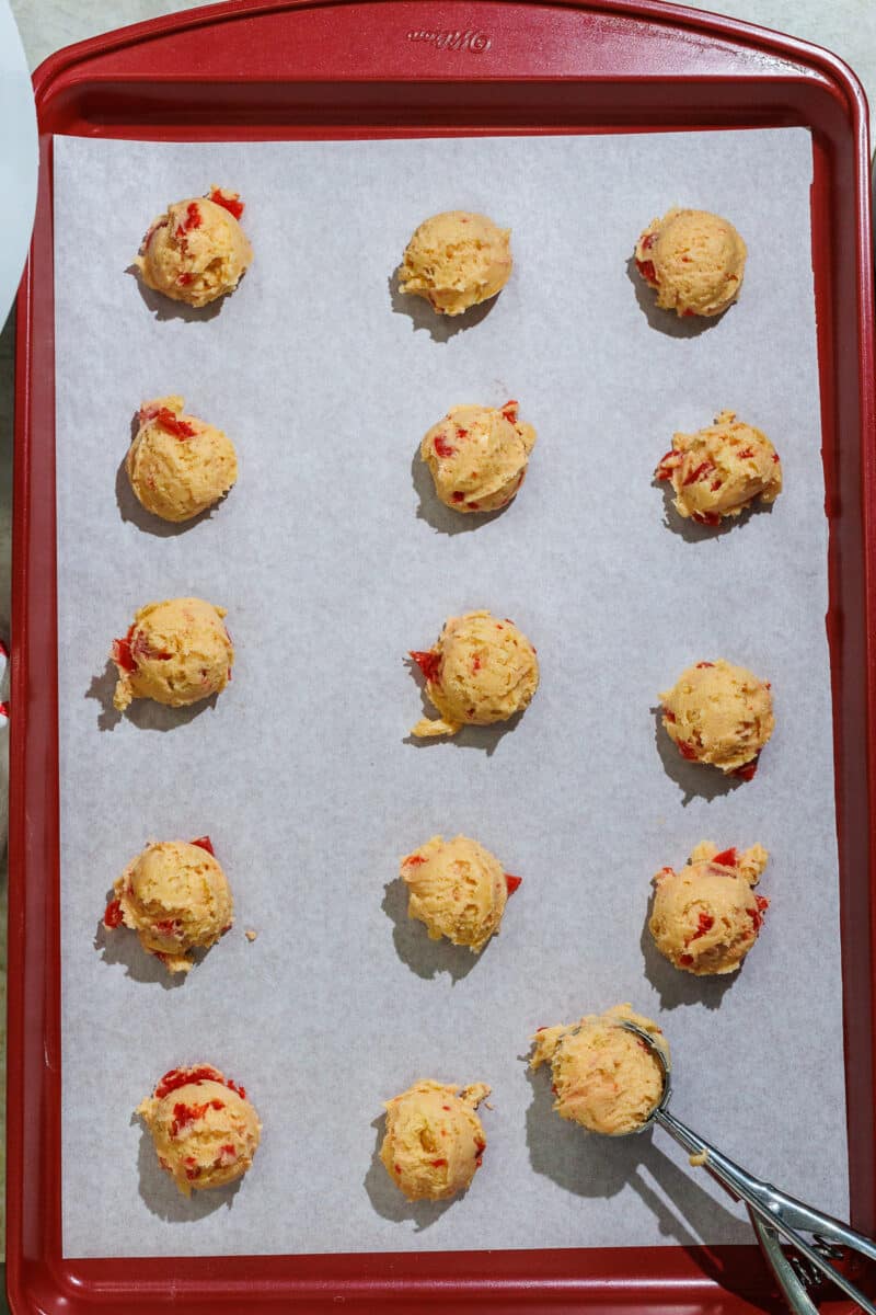 cherry cookie dough balls on parchment paper on a red wilton cookie sheet