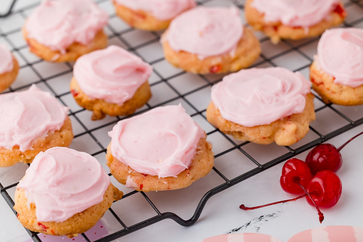 cherry cookies frosted with cream cheese and almond frosting on a cooling rack