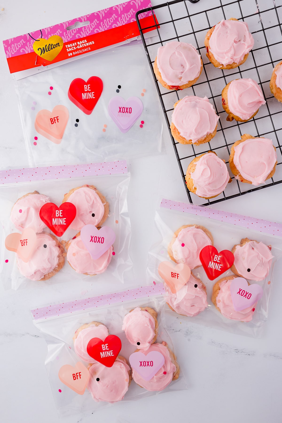 cherry cookies with pink frosting on a wire rack and wilton treat bags for Valentine's Day