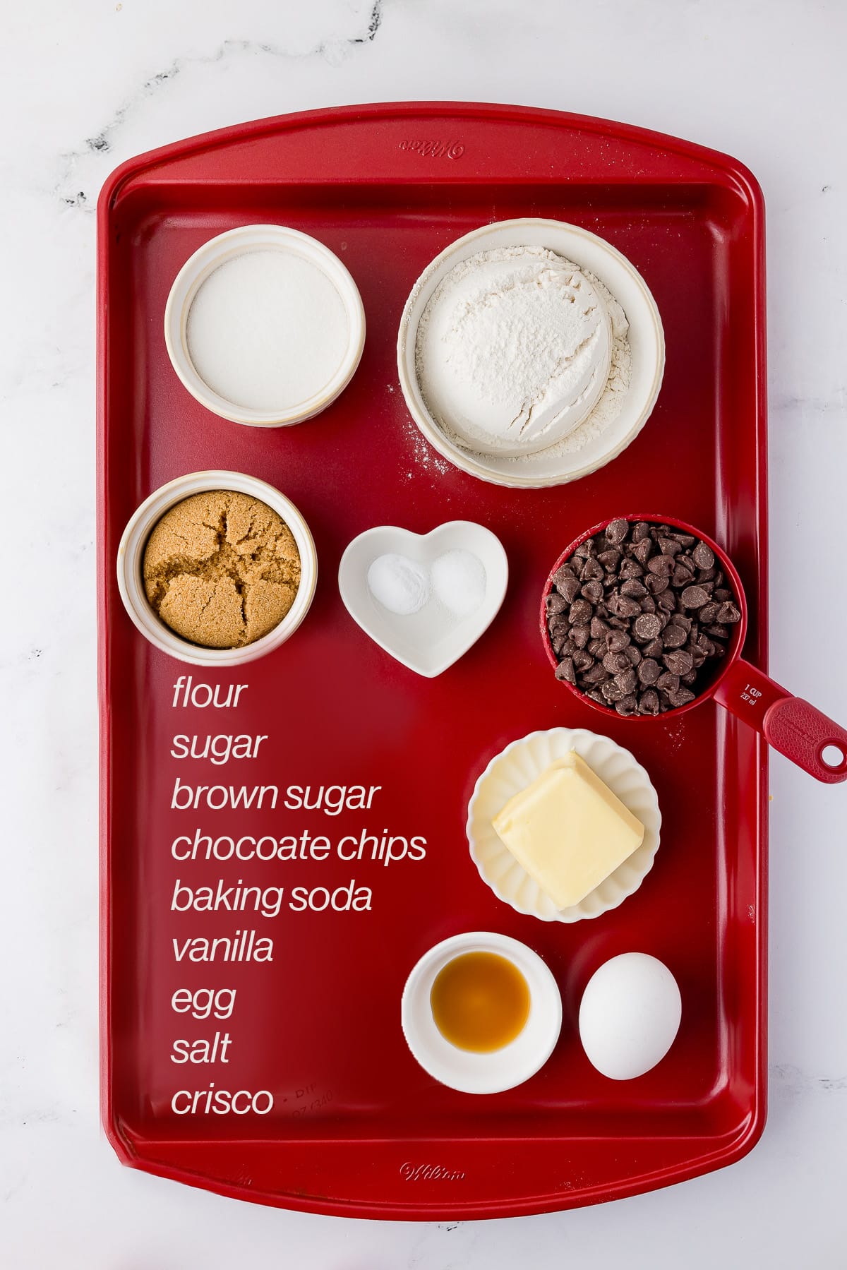 ingredients for chocolate chip cookies on a red cookie sheet