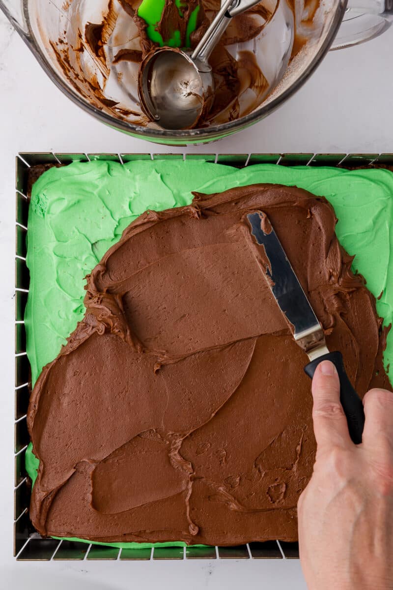 spreading chocolate frosting on top of mint brownies