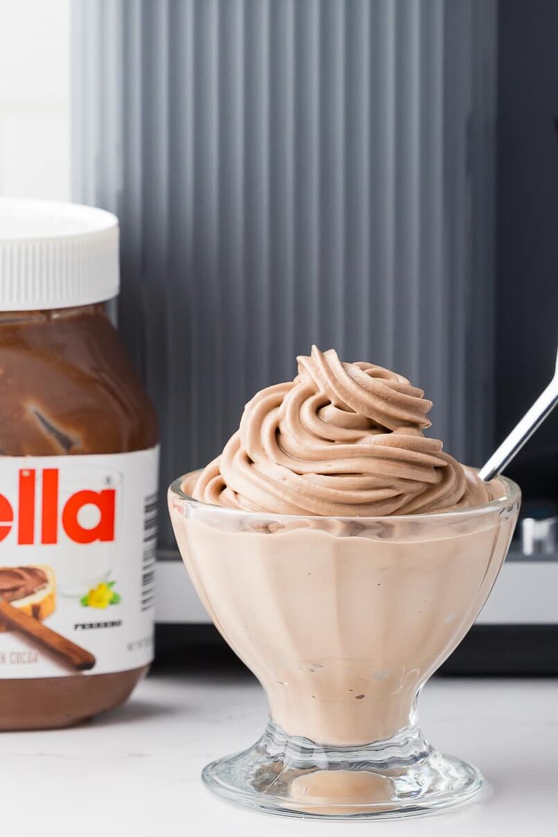 nutella soft swerve ice cream in a sundae bowl in from of the ninja swirl by creami with a heart spoon with a jar of nutella