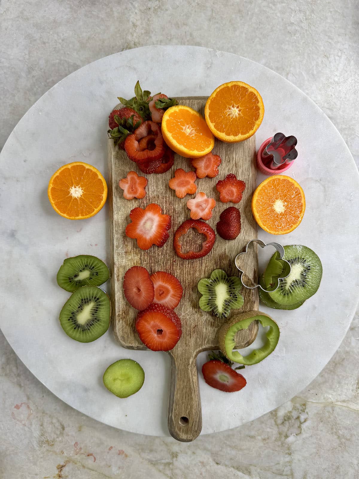 Kiwi, oranges and strawberries cut up on a cutting board with a knife