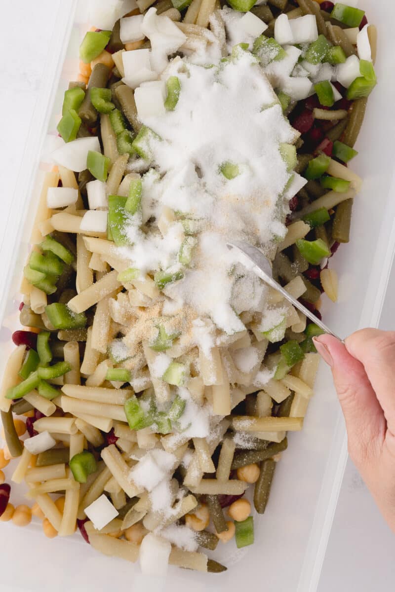 adding garlic to tupperware rectangular dish with beans, onions, and green peppers on a white countertop