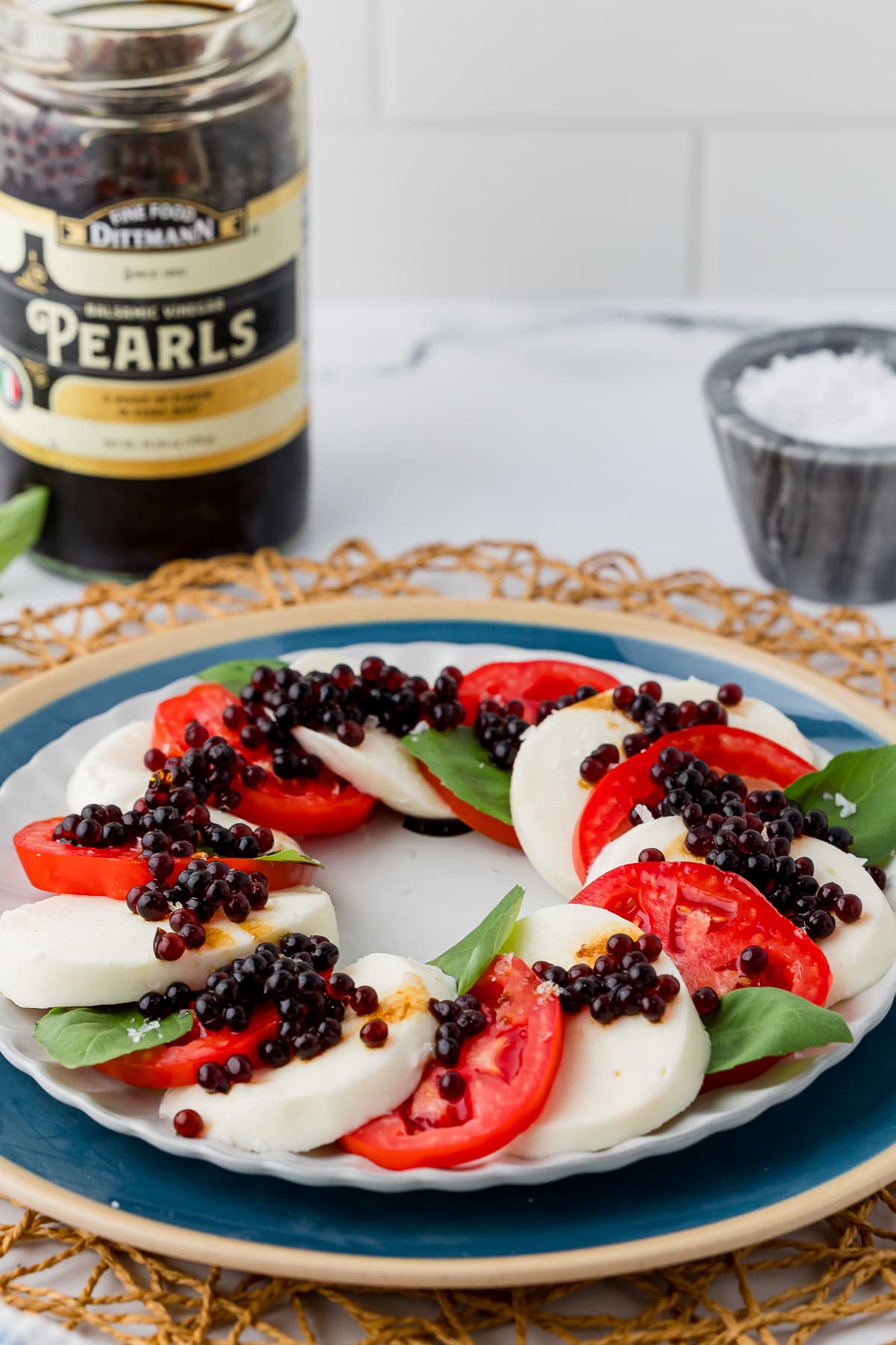 Sliced cheese, tomatoes and fresh basil leaves topped with balsamic pearls on an appetizer plate