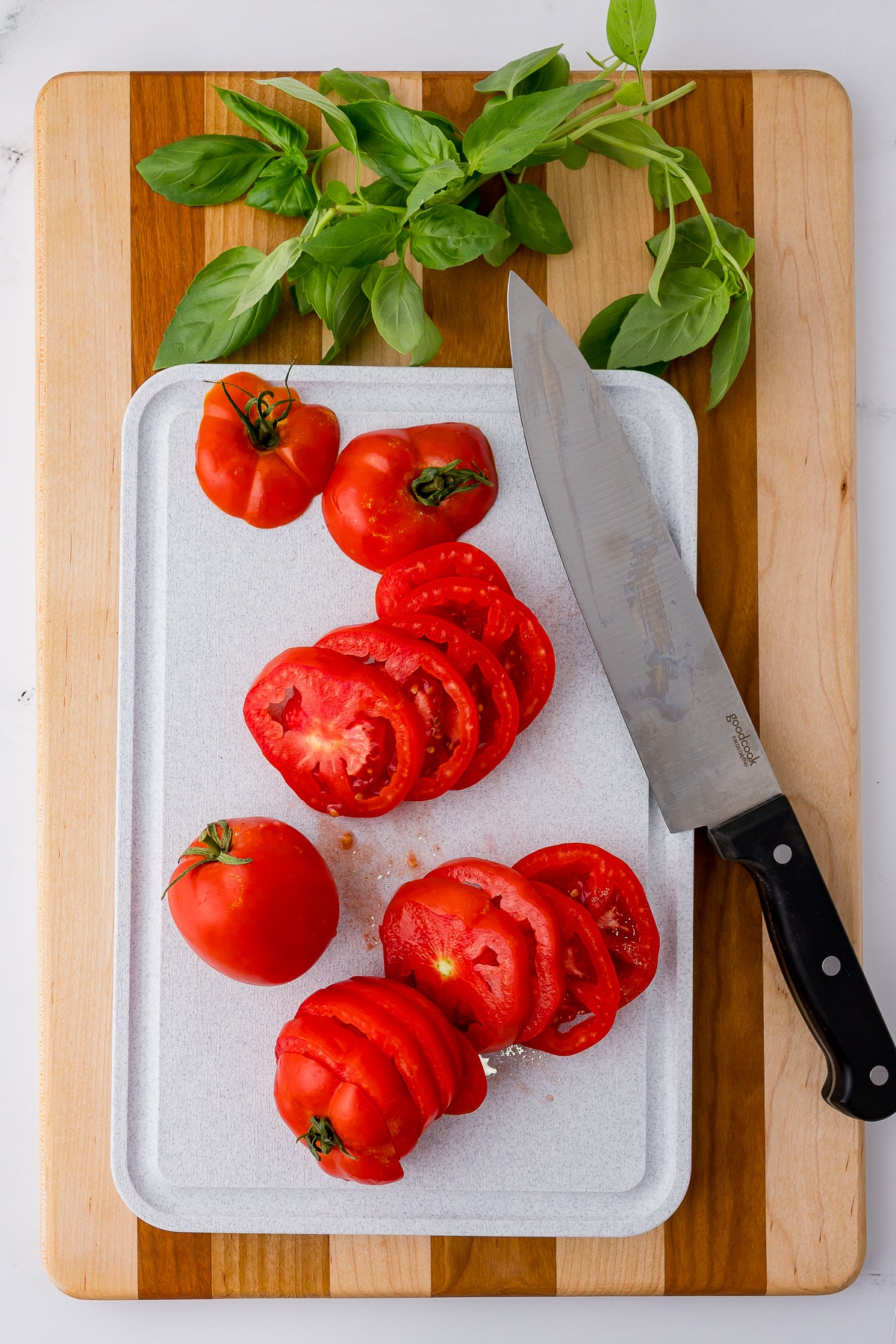Tomato slices on a cutting board with a large knife and basil leaves in the background