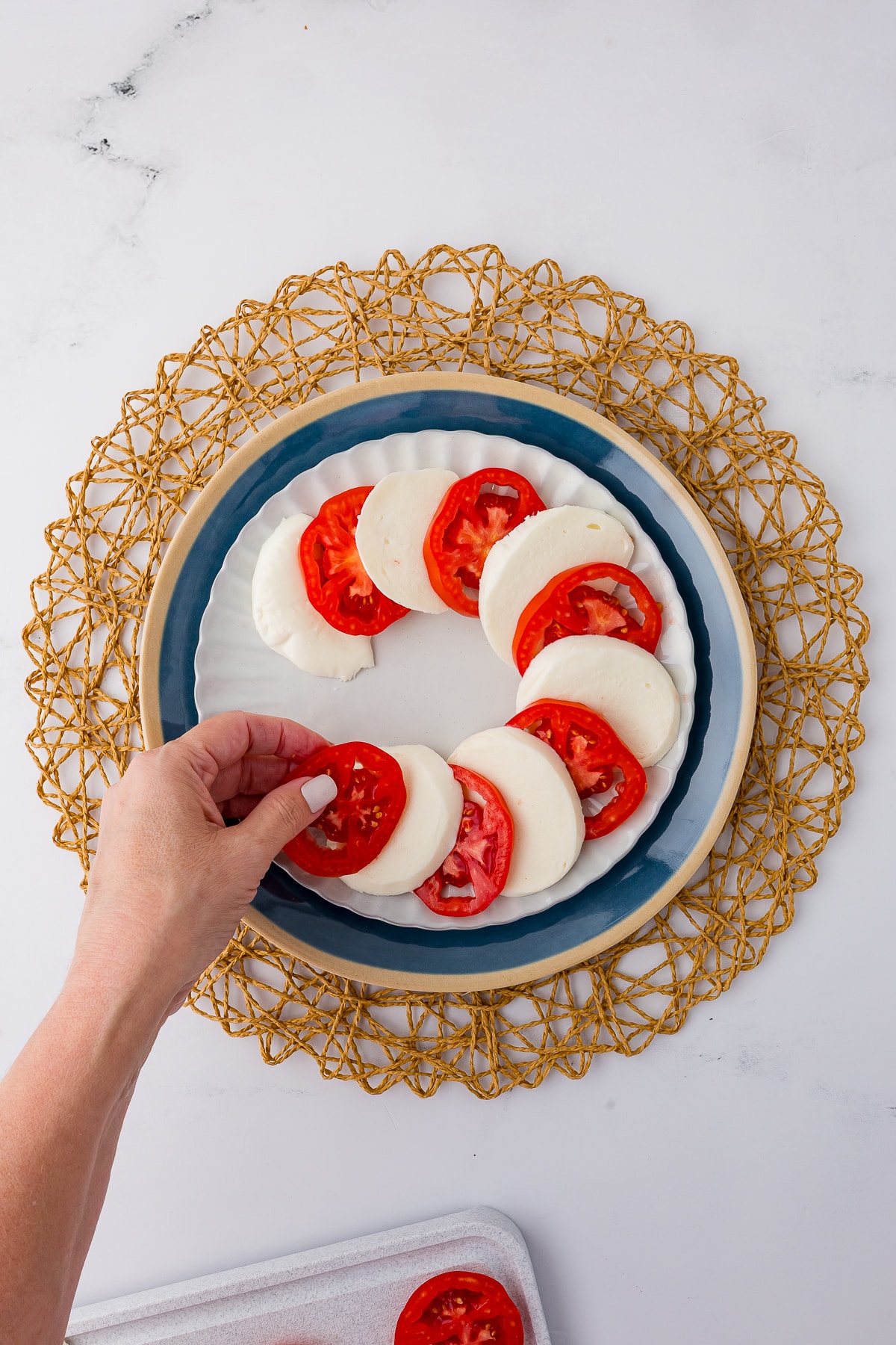 A hand layering mozzarella slices with tomato slices on a plate