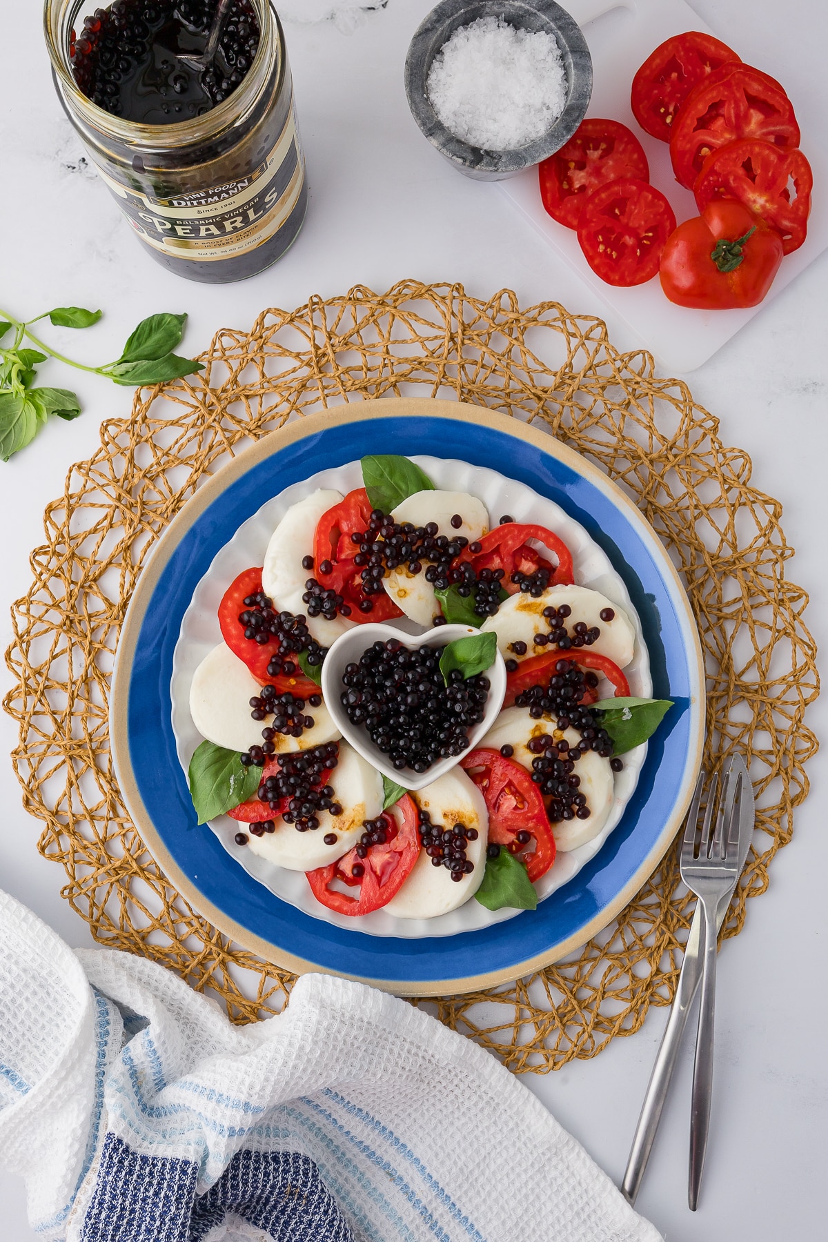 Lovely shot of a caprese salad appetizer tray with a heart shaped bowl of balsamic vinegar pearls in the middle
