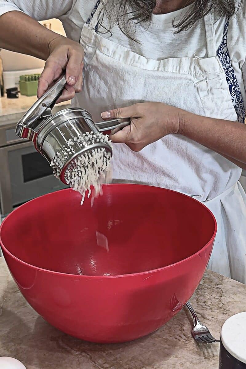 hot cooked russet potatoes being passed through a ricer into a red bowl