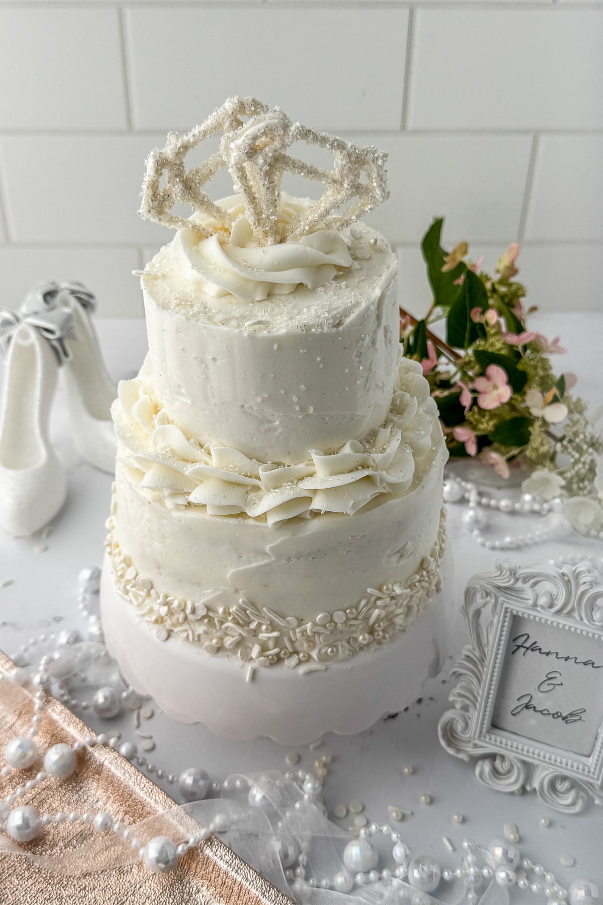 mini white wedding cake on a white counter with flowers, and pearl decorations