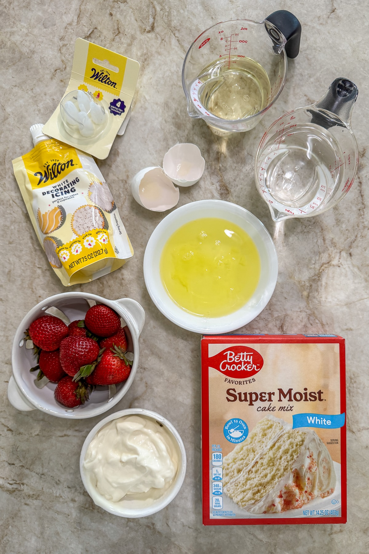 oil, water, egg whites, betty crocker super moist white came mix, strawberries, wilton white deocrating icing, and greek yogurt on a marble countertop