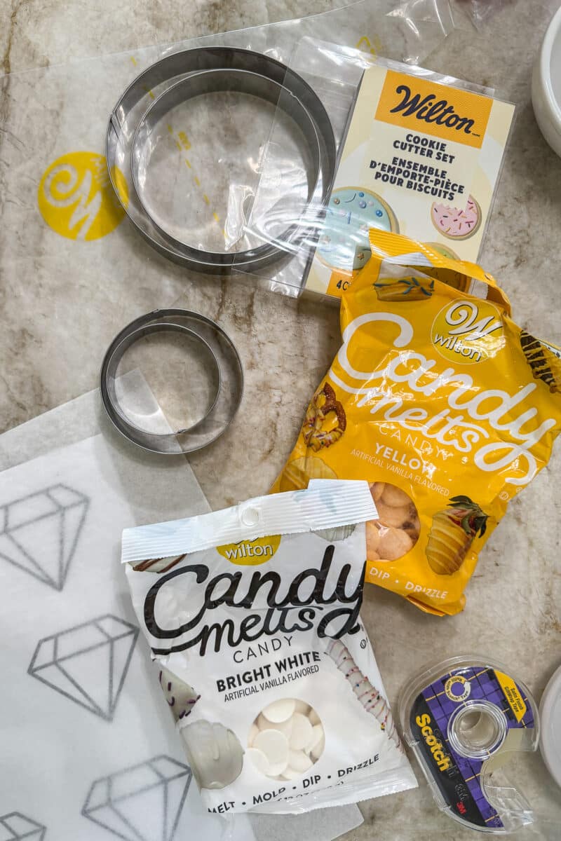 wilton cookie cutter set, wilton candy melts, scotch tape, and parchment paper on a marble countertop
