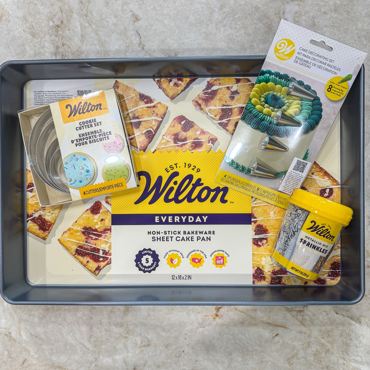 Wilton sheet cake pan, wilton cake decorating set, wilton cookie cutter set, wilton metallic mix sprinkles on a marble countertop
