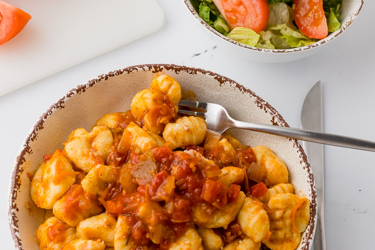 potato ñoquis with tomato pasta sauce in a pasta bowl on a white counter