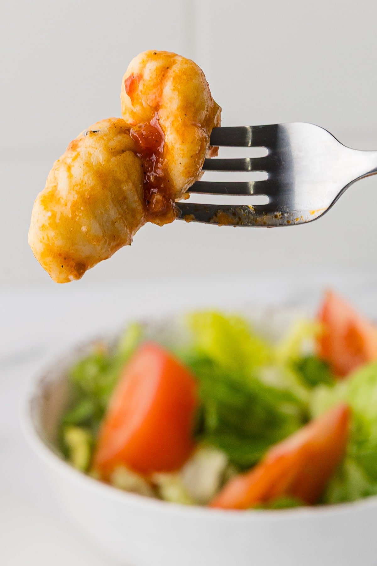 closeup of two noquis on a fork with a side salad in the background