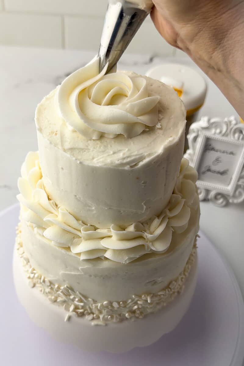 piping a rosette on top of a mini engagement cake