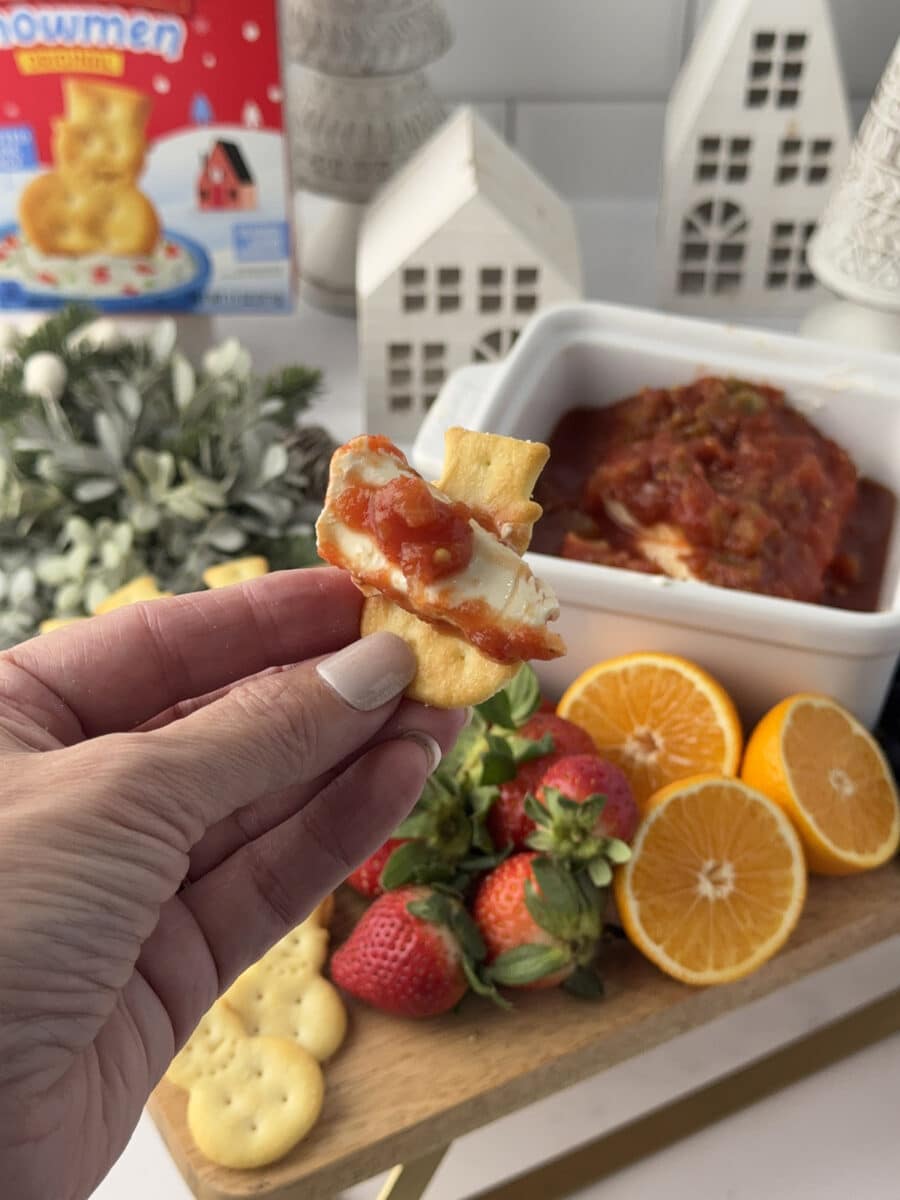 hand holding snowman cracker with salsa and cream cheese
