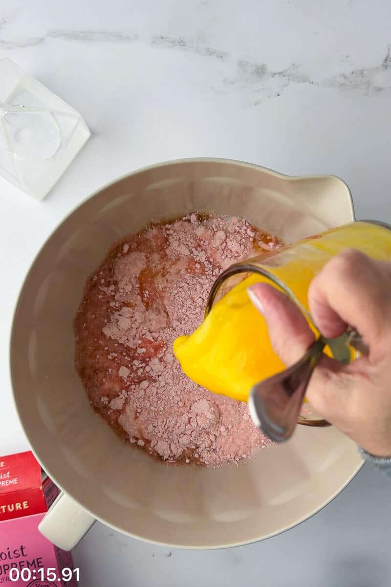 Pouring melted butter into a batter bowl with strawberry cake mix