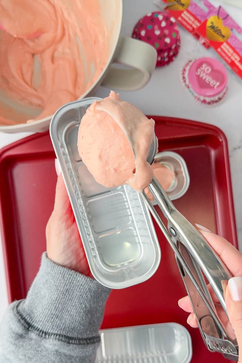 scooper pouring strawberry cake mix into mini loaf pan