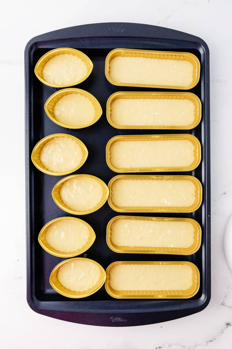 football shaped cupcakes and mini loaf pans filled with yellow cake batter on a wilton cookie sheet