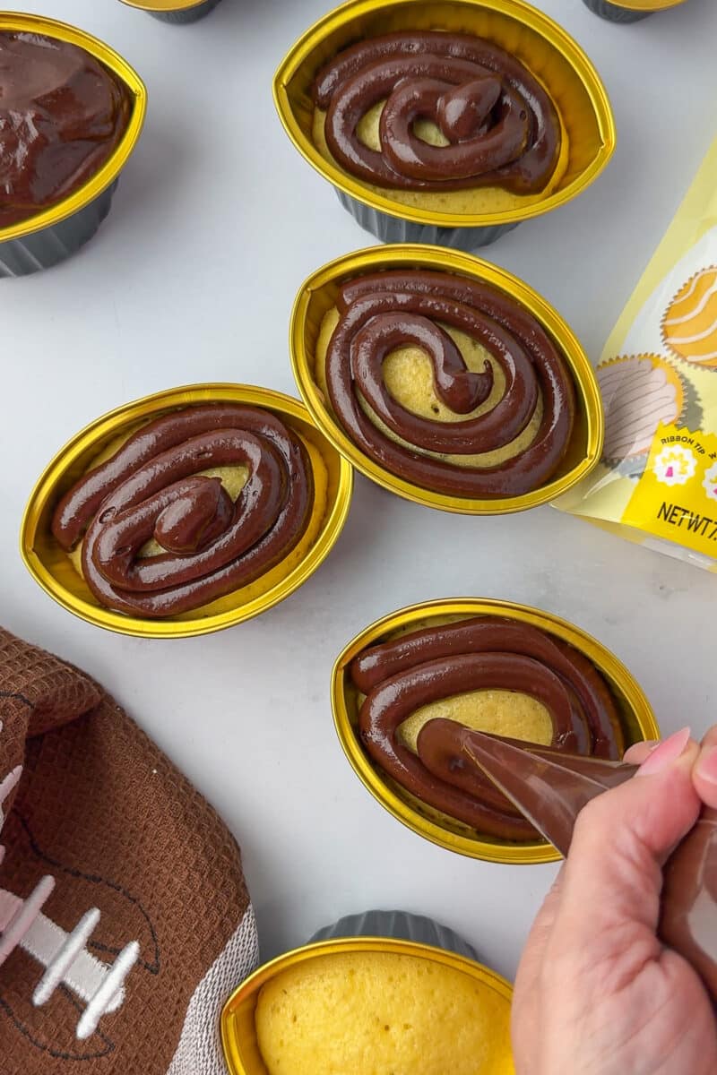 piping chocolate frosting on football shaped cupcakes