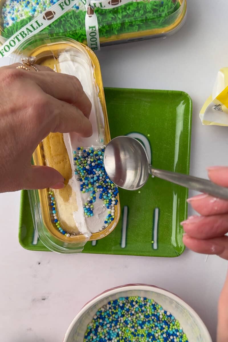 spreading green blue and white sprinkles on a mini loaf pan to resemble fans in the stands