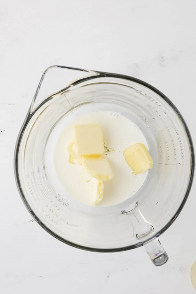 Cubes of yellow softened butter sitting in a glass mixing bowl with a small amount of milk, ready to be whipped for frosting.