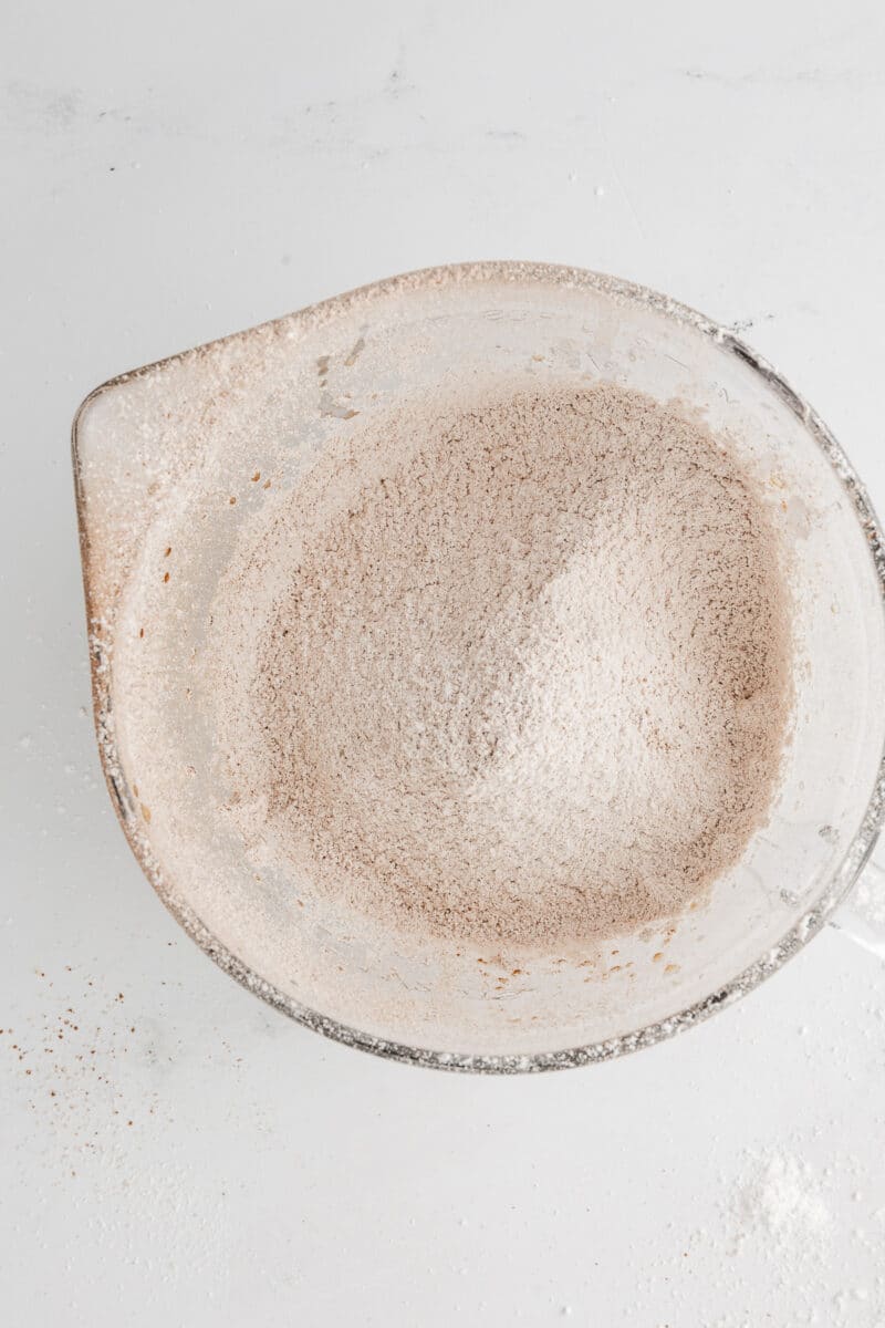 A glass mixing bowl containing finely sifted powdered sugar and cocoa powder, ready to be incorporated into the whipped butter base.