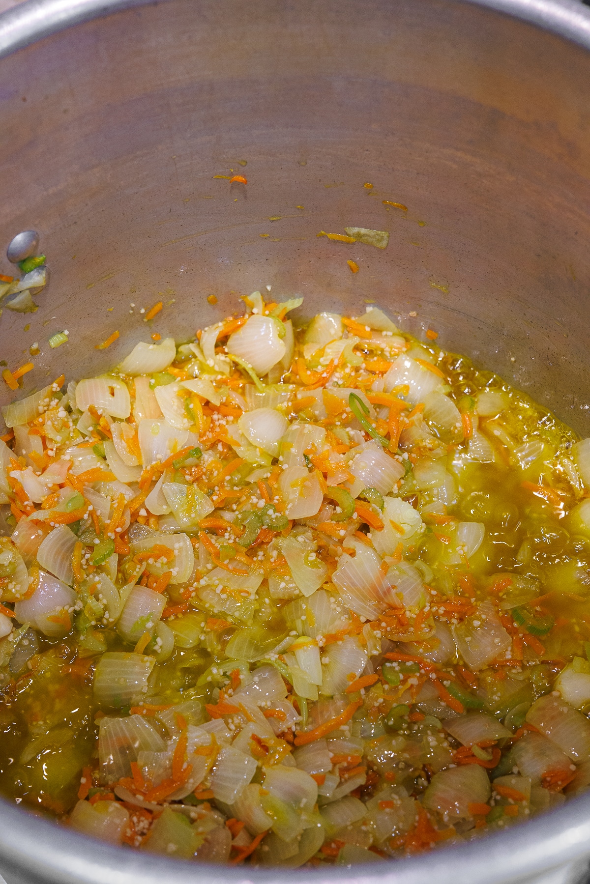 Minced garlic granules sprinkled over sautéed vegetables in a large metal pot.